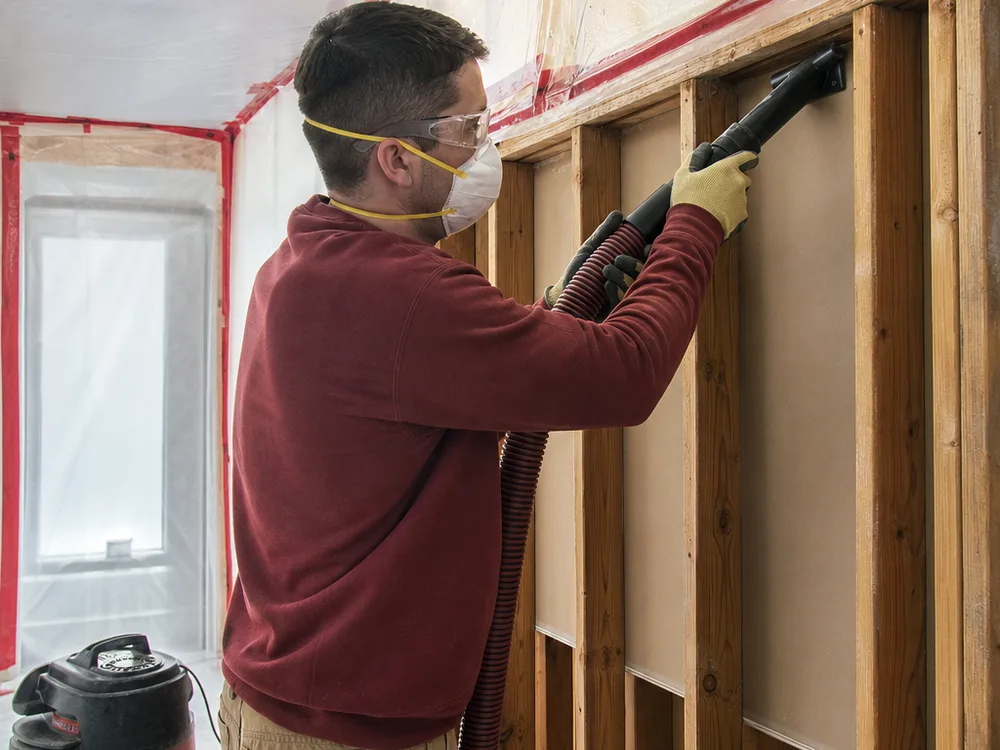 Contractor using a HEPA vacuum on exposed wall studs inside a contained work area